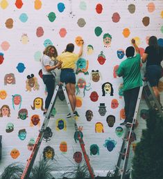 three people are painting on a wall with many different colored circles around them and one person is standing on a ladder