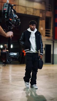 a young man is standing in front of a camera and holding a bag while wearing a black jacket