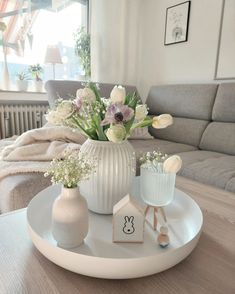 a white vase with flowers on a table in front of a couch and coffee table