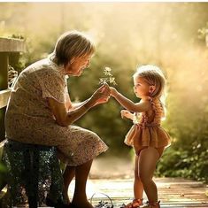 an older woman holding a small child's hand while sitting on a wooden bench