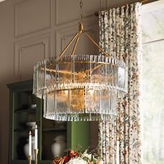 a chandelier hanging over a dining room table with flowers and candles on it