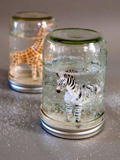 two glass jars with animals in them sitting on a counter top, one is filled with water and the other has a giraffe figurine