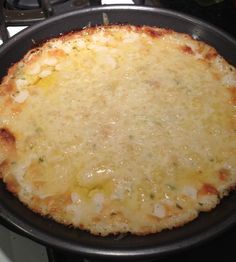 a cheese pizza sitting on top of a stove next to a frying pan filled with food