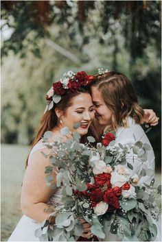 two women are hugging each other with flowers in their hair and one is holding a bouquet