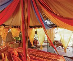 a bed with red, yellow and blue drapes on it's sides in a tent