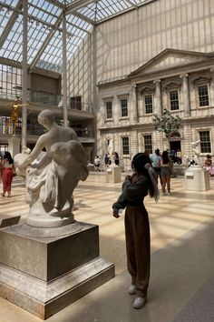 a woman is looking at a statue in a large room with many windows and people walking around