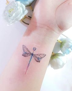 a small tattoo on the wrist of a woman's arm with a blue dragonfly