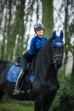 a woman riding on the back of a black horse in front of some tall trees