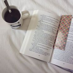 an open book next to a cup of coffee on top of a white bed sheet