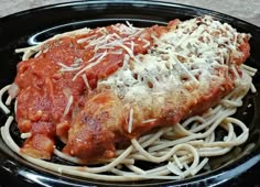 a black plate topped with pasta and meat covered in sauce, parmesan cheese