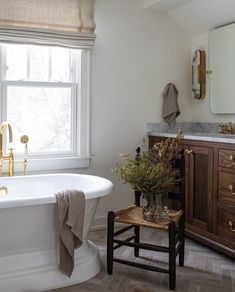 a white bath tub sitting next to a wooden cabinet in a bathroom under a window