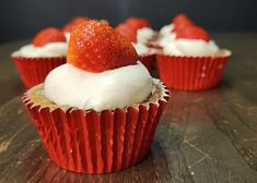 some cupcakes with white frosting and strawberries on top are sitting on a table