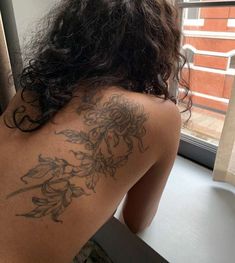 a woman with a tattoo on her back looking out the window