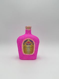 a pink glass bottle with gold trimmings and a crown on the top, sitting in front of a white background