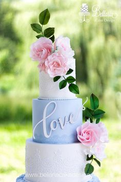 a three tiered cake with pink flowers on top and the word love painted on it