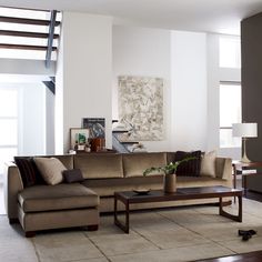 a living room filled with furniture and a stair case in the back ground floor to ceiling windows