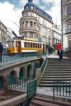 a yellow and white train traveling down tracks next to tall buildings with people walking on the sidewalk