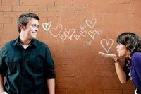 two people standing in front of a brick wall with hearts drawn on it and pointing at each other