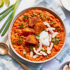 a bowl filled with rice and meat on top of a blue table cloth next to silver spoons