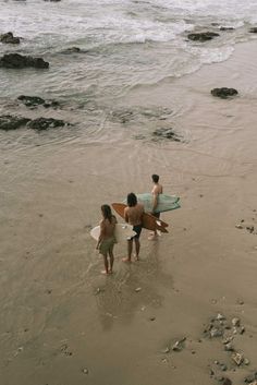 three people walking on the beach with surfboards in their hands and one person holding a surfboard