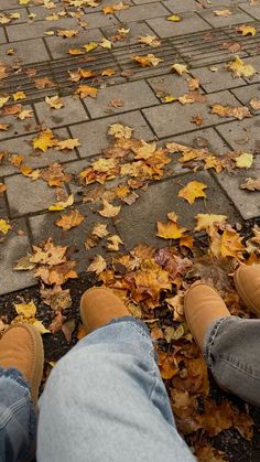 two people sitting on the ground with their feet up in front of them, surrounded by leaves