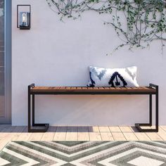 a bench sitting in front of a white wall with a plant on top of it