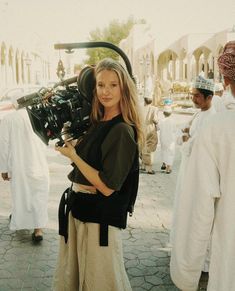 a woman holding a camera in front of other people on the street with others behind her