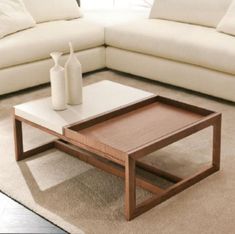 a coffee table with two vases on it in front of a white sectional couch