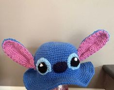 a crocheted blue hat with pink ears and eyes on top of a wooden table