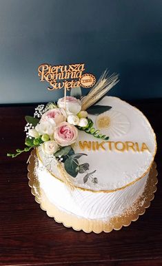 a white cake with gold lettering and flowers on the top is sitting on a wooden table