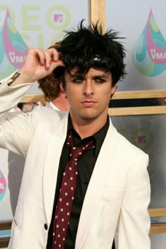 a man in a white suit and tie with black hair wearing a red polka dot tie