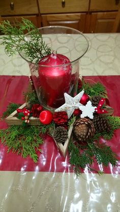 a candle and some pine cones on a red table cloth with christmas decorations around it