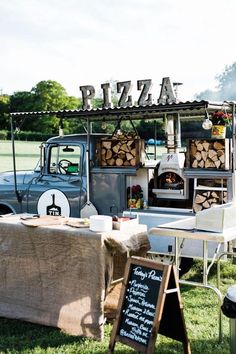 a pizza truck parked in the grass near a table