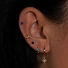 a woman wearing ear piercings with blue and white stones on her left ear, in front of black background