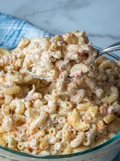 a glass bowl filled with macaroni salad on top of a blue towel next to a spoon