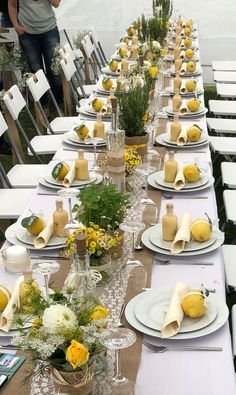 a long table is set with white plates and yellow flowers