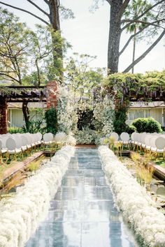 an outdoor ceremony with white chairs and flowers on the aisle, surrounded by greenery