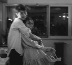 black and white photograph of two people hugging each other in the kitchen at night time