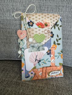 an open envelope with flowers on it and some tags attached to the front, sitting on top of a couch