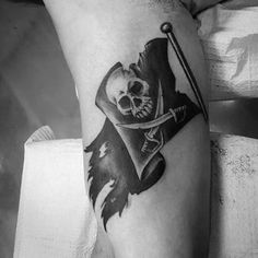 a black and white photo of a skull with a pirate flag tattoo on his leg