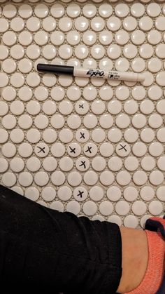 a person standing in front of a tiled wall with writing on it and a pen