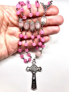 There are 59 total beads in this five decade rosary. The rosary has a 2 Inch Silver Plated St. Benedict Crucifix that is beautifully detailed on both sides. The center is an antiqued silver plated fancy scrolled 3-way. This rosary is wired wrapped with very nice 6 mm faceted pink jade in unbreakable fashion. There are 24 silver plated bead caps that protect the beautiful Rose Quarts Oval Beads that represent the Pater (Our Father) Beads. ROSE QUARTZ: The fair and lovely Rose Quartz, with its gen Handmade Pink Rosary For Healing, Pink Healing Rosary With 8mm Beads, Spiritual Rosary With Spacer Beads, Pink Rosary With 8mm Round Beads, Pink Beaded Spiritual Rosary, Pink Spiritual Rosary Bracelet With 8mm Beads, Pink 8mm Bead Spiritual Rosary Bracelet, Pink 8mm Beads Rosary Bracelet, Pink Rosary Bracelet With Round Beads For Healing