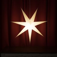 a white star hanging from a red curtain in front of a dark room with curtains