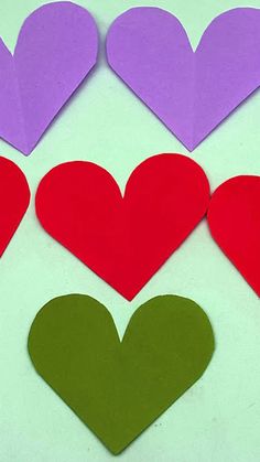 paper hearts arranged in different colors on a white surface with green and purple ones next to each other