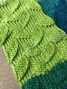 a green and blue knitted blanket laying on top of a floor next to a rug