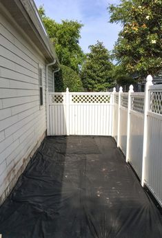 a white fence with a black tarp covering the area in between it and a house