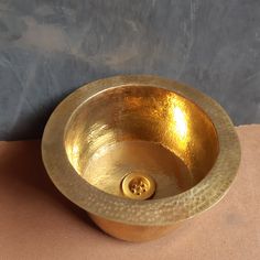 a gold bowl sink on top of a tan table cloth next to a gray wall