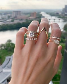 a woman's hand with two rings on top of her finger and the view of a river in the background