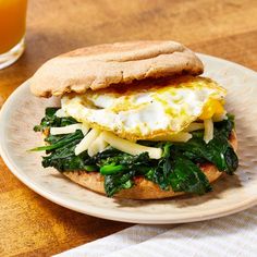 an egg, cheese and spinach sandwich on a plate with a glass of orange juice