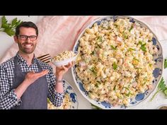 a man holding a bowl of macaroni salad next to a platter full of macaroni and cheese